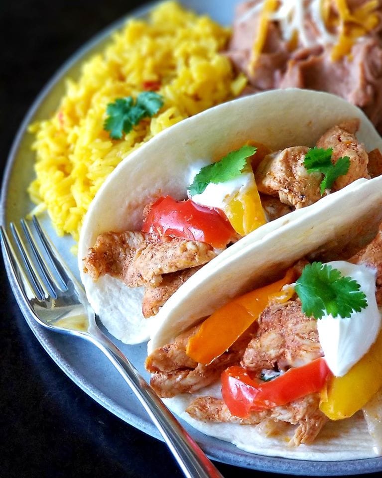chicken fajitas served on a plate with yellow rice and refried beans