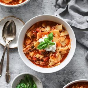a heart bowl of lasagna soup with a dollop of sour cream on the top and fresh basil