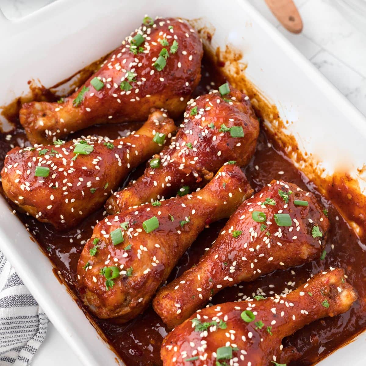 6 bbq drumsticks in a sweet bbq sauce baked in a white casserole dish.