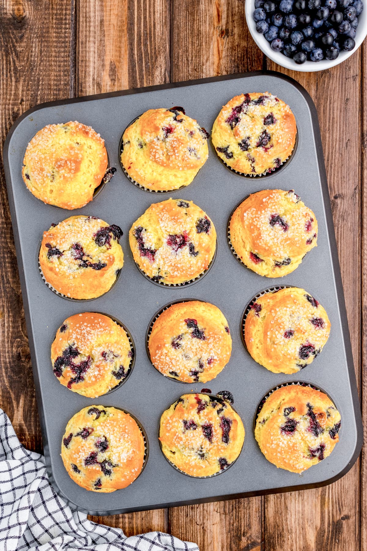 Freshly baked lemon-blueberry muffins cooling on a wire rack, with a golden-brown top and sparkling sugar glisten.