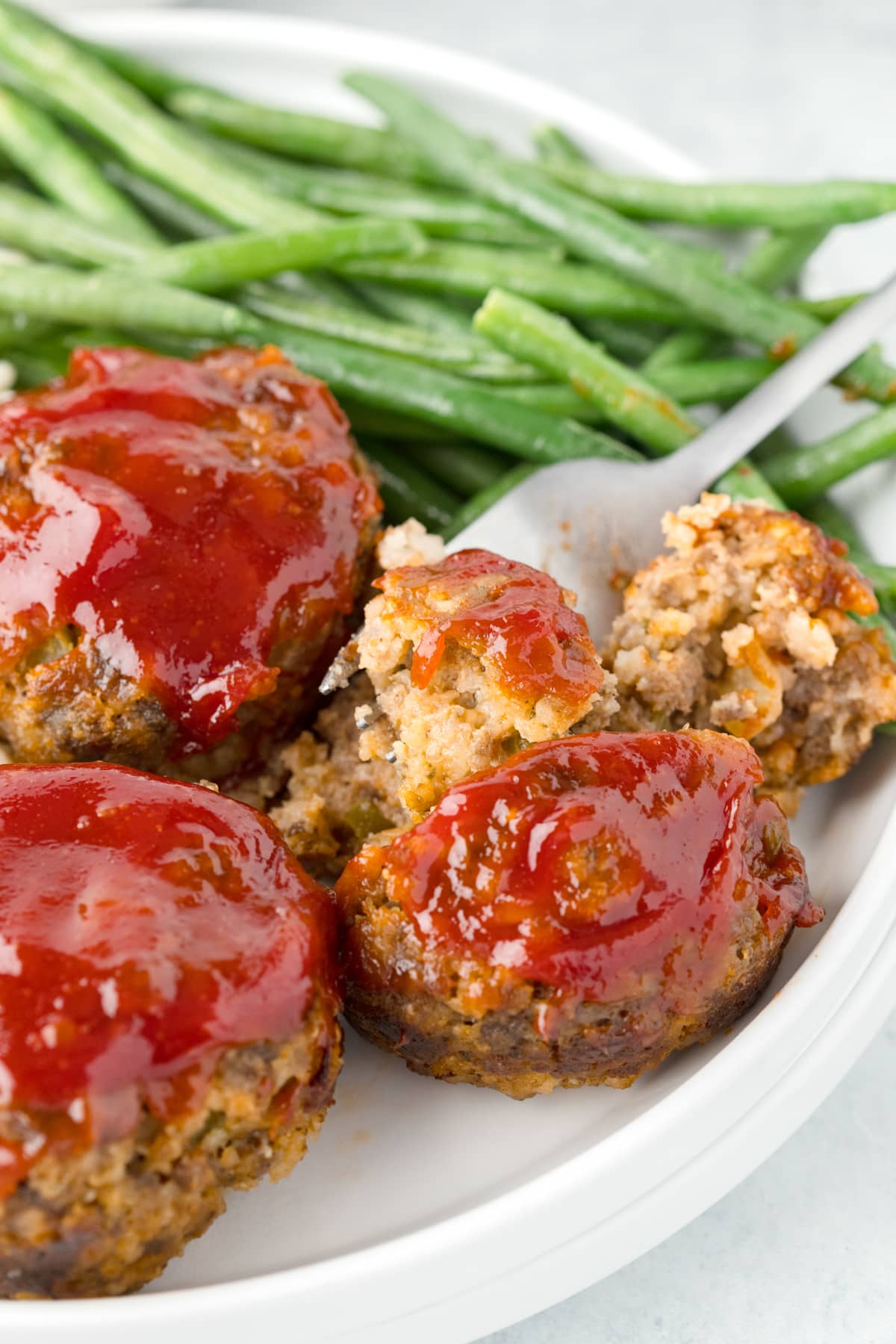 mini meatloaf muffins on a white plate with a fork tearing one muffin in half, served with green beans.
