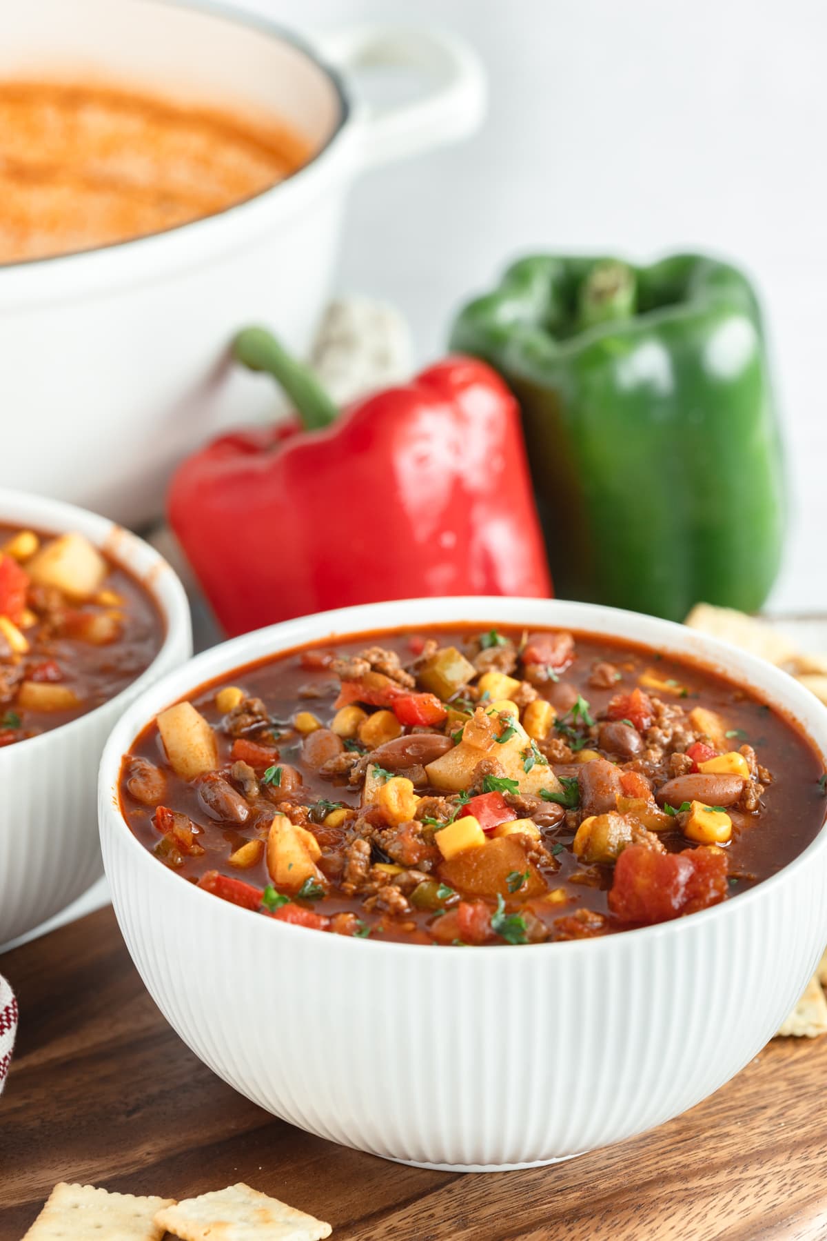 A white bowl filled with cowboy, and one is offset to the left with a large white dutch oven in the background with red and green bell peppers.
