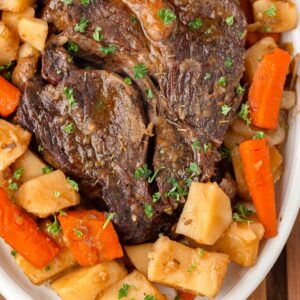A close up of a cooked pot roast surrounded by potatoes and carrots.