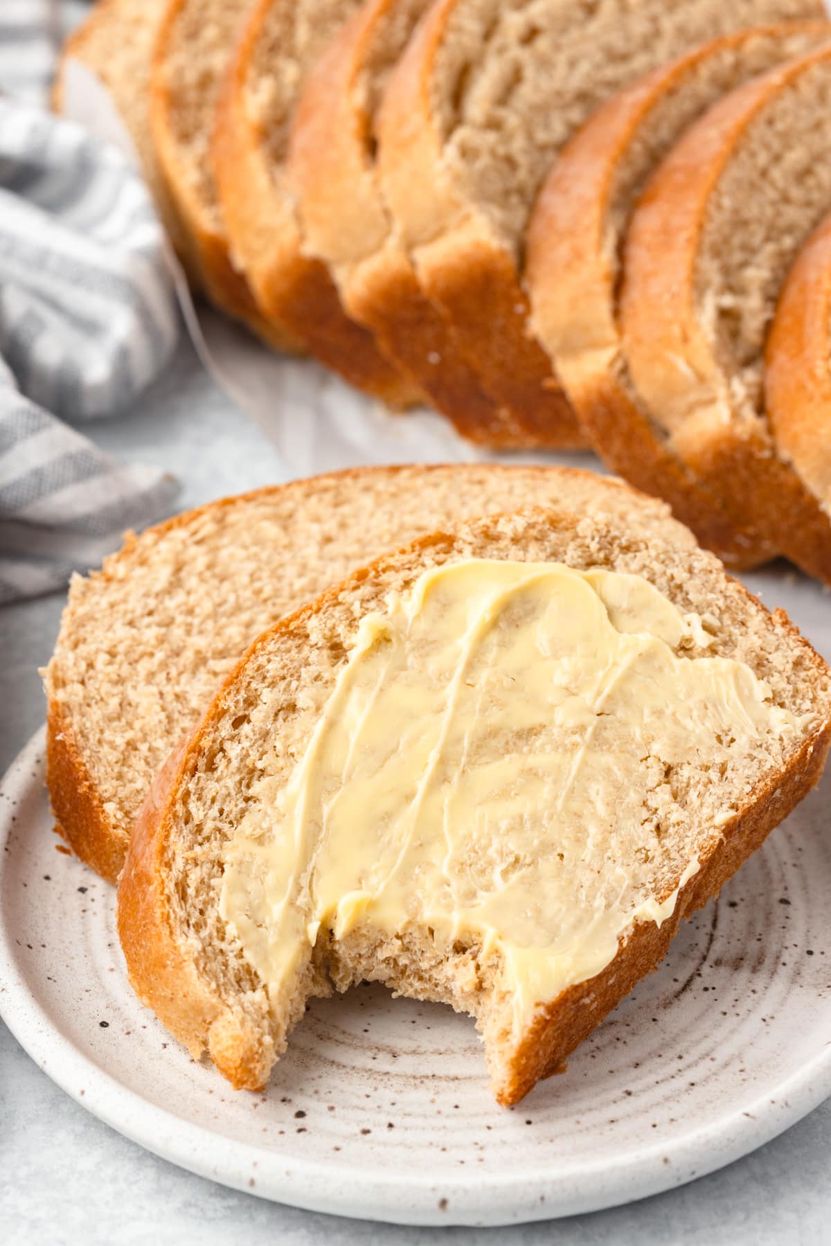 Two slices of bread on a small speckled plate, slathered in butter. One slice has a bite taken out of it.