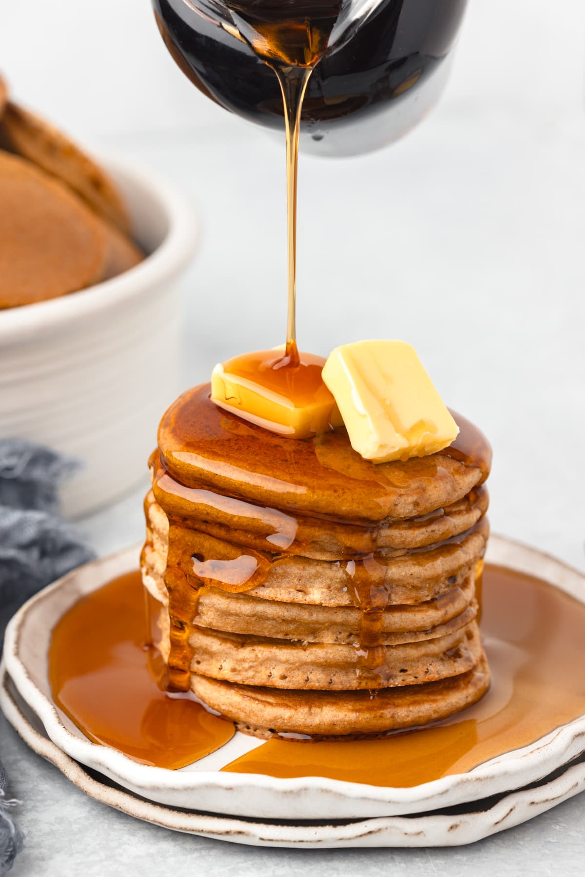 A stack of whole wheat pancakes with butter on top and syrup being poured on the top.
