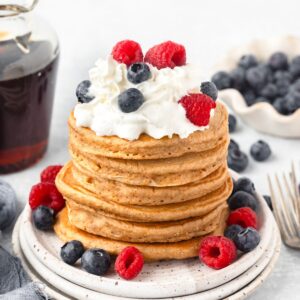 Whole Wheat Pancakes stacked on little plates topped with whipped cream and fresh berries.