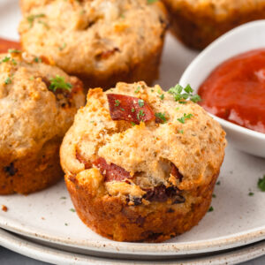 Pizza muffins on stacked plates with a side of pizza sauce in a little white dish.