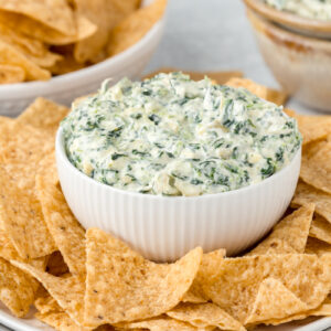 Spinach and artichoke dip in a white bowl surrounded by tortilla chips.
