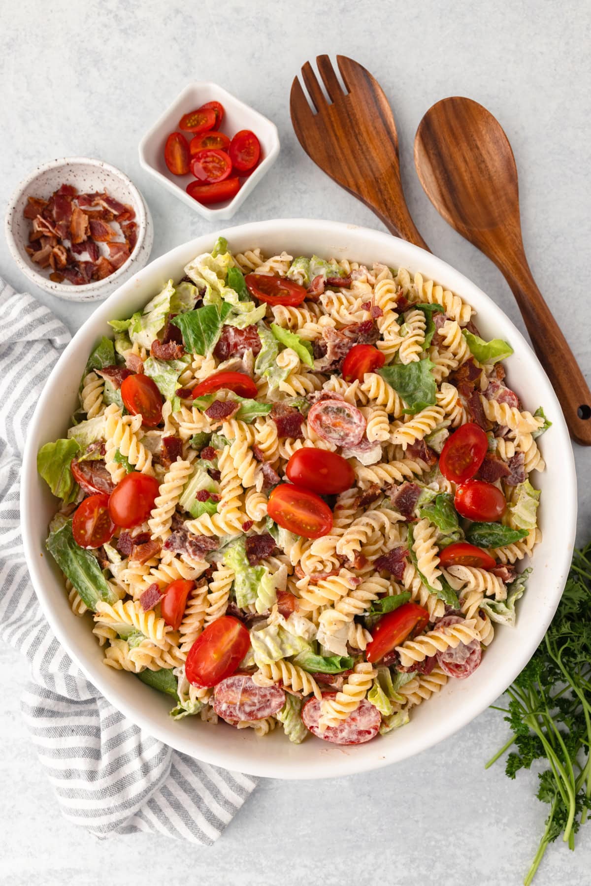 A large white bowl containing a blt pasta salad. It has bacon, romaine lettuce and grape tomatoes.