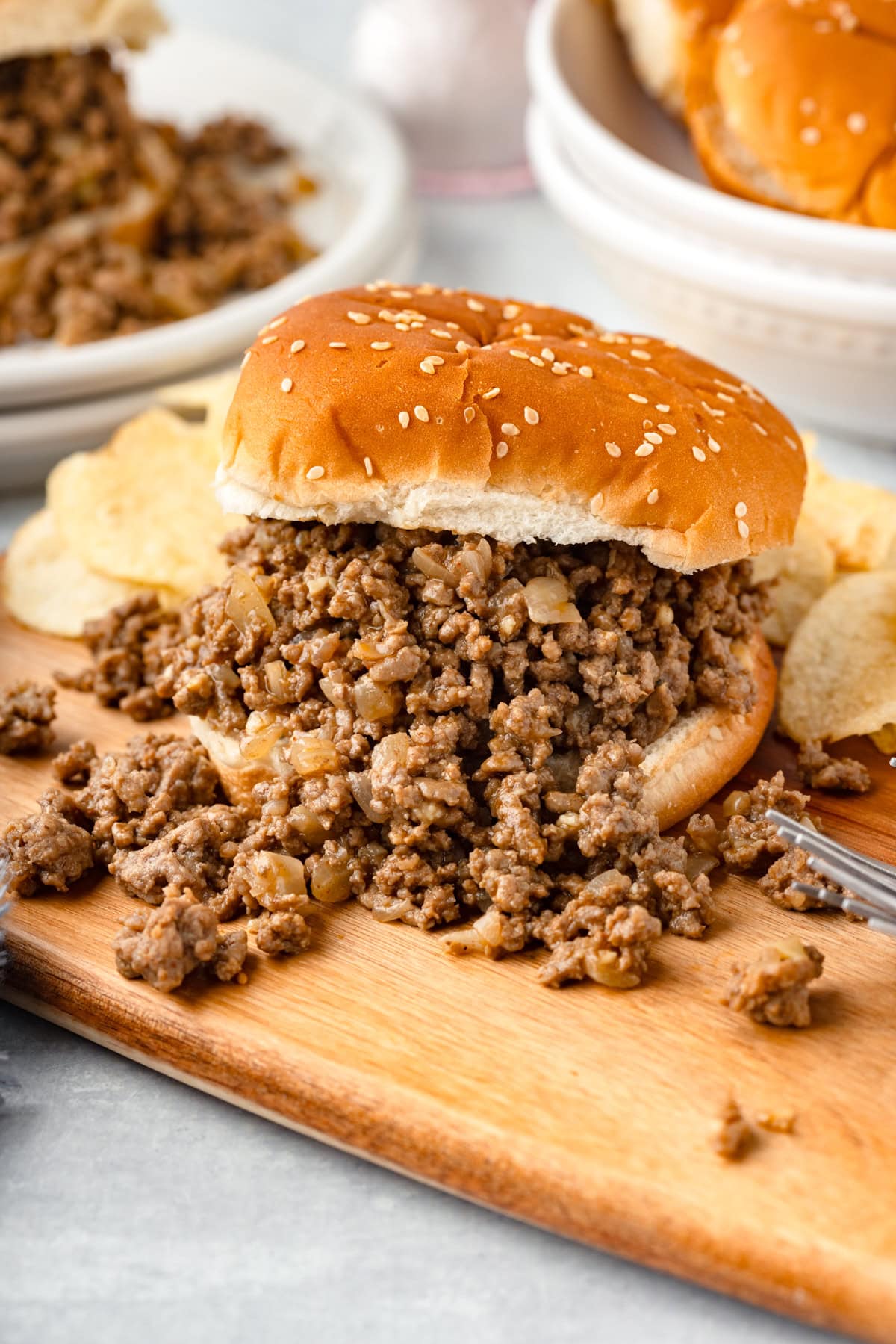 Seasoned, cooked ground beef on a hamburger bun with it spilling over onto a wood cutting board.