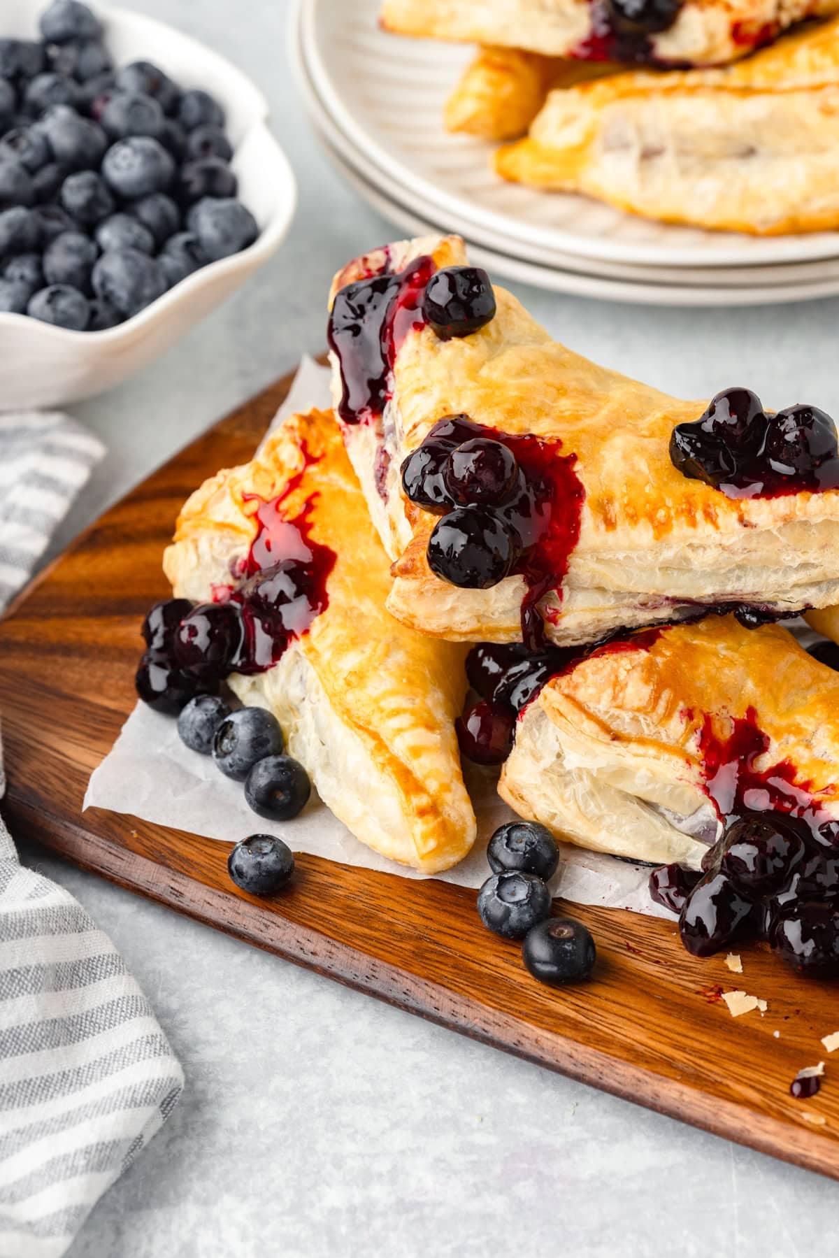 Three blueberry turnovers stacked on a wood cutting board.