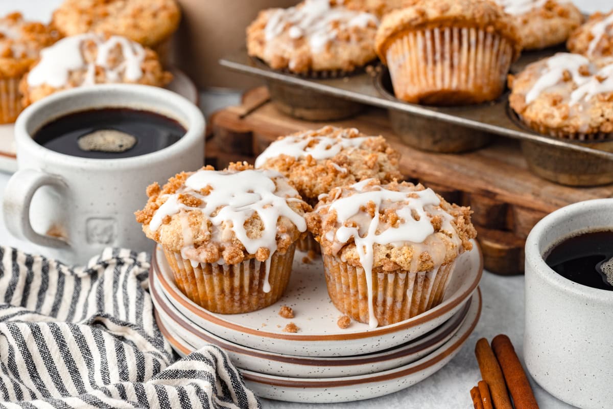 Sweet cinnamon streusel muffins with white icing drizzle and cups of black coffee on a rustic table.