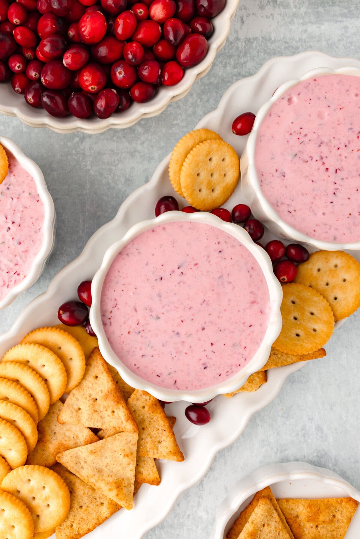 Fresh cranberry dip with crackers and cookies on a white platter, served with a bowl of fresh cranberries.