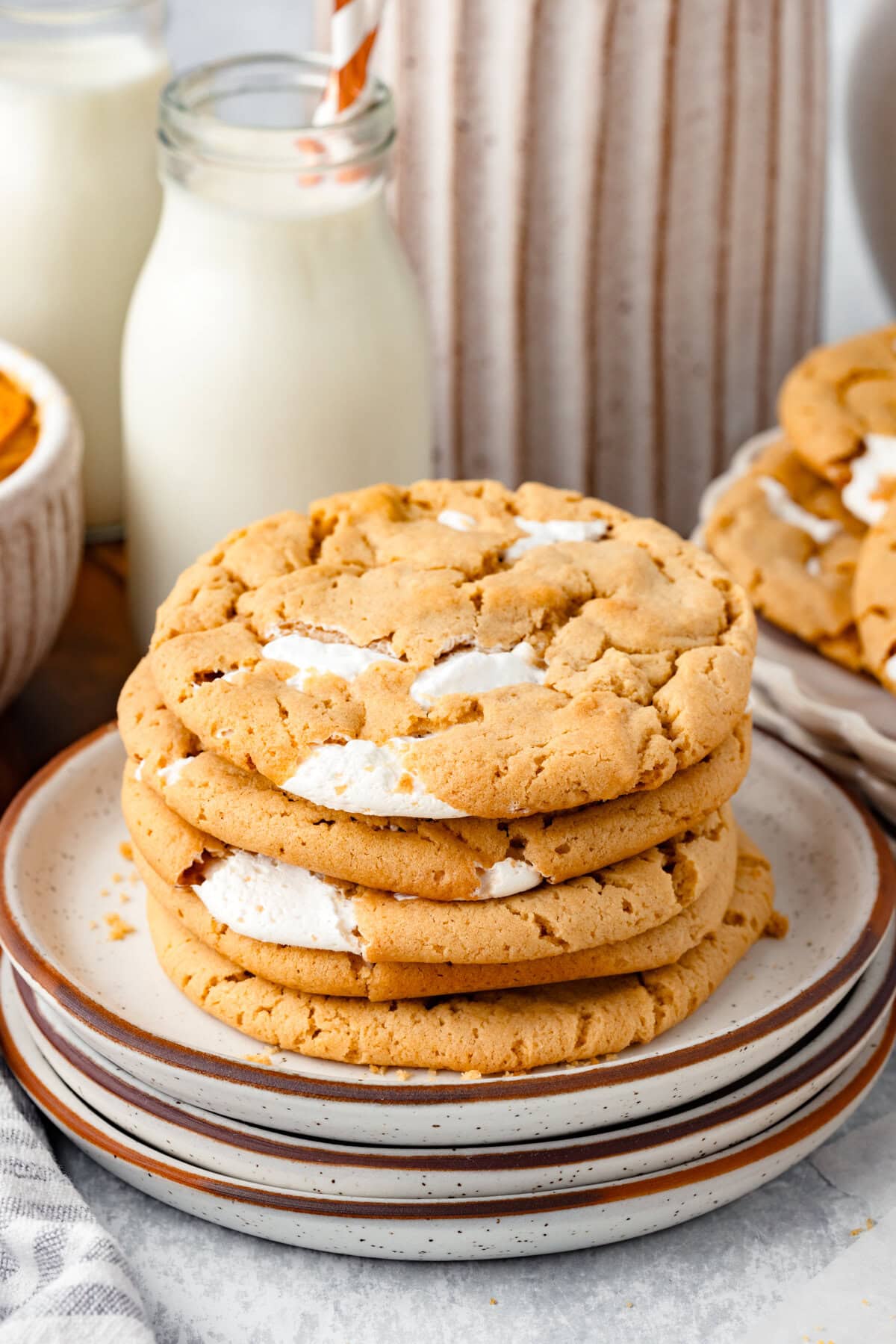 Buttery chocolate chip cookies with creamy white filling on stacked plates.