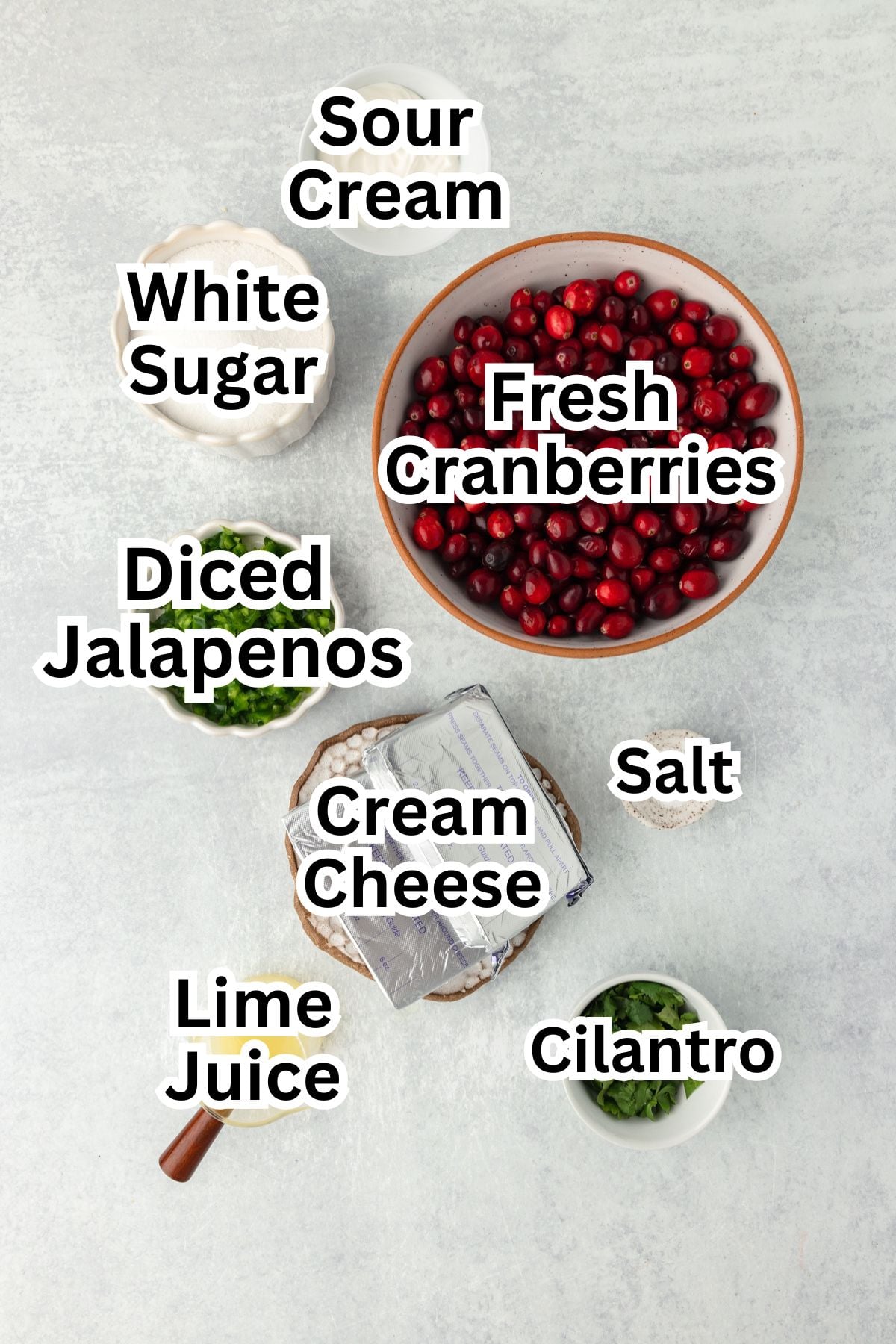 Fresh cranberries in a bowl with other ingredients for a recipe, including sour cream, sugar, diced jalapenos, cream cheese, lime juice, salt, and cilantro.