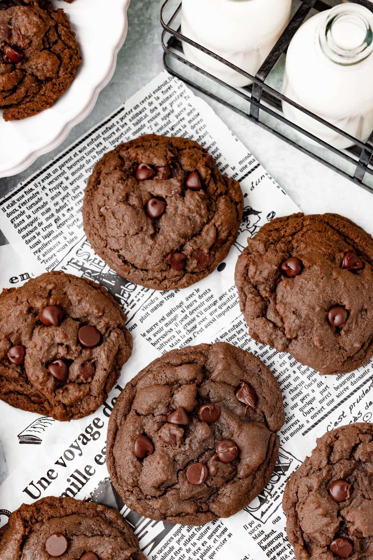 Chocolate chip cookies on newspaper print with milk bottles in the background.