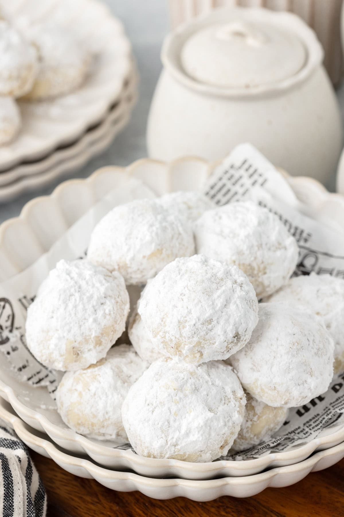 Powdered sugar coated cookies in a white bowl, with a milk jug in the background.