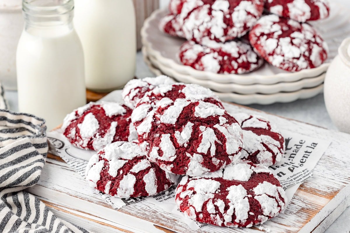 Crimson crinkle cookies with powdered sugar on rustic white wooden board.