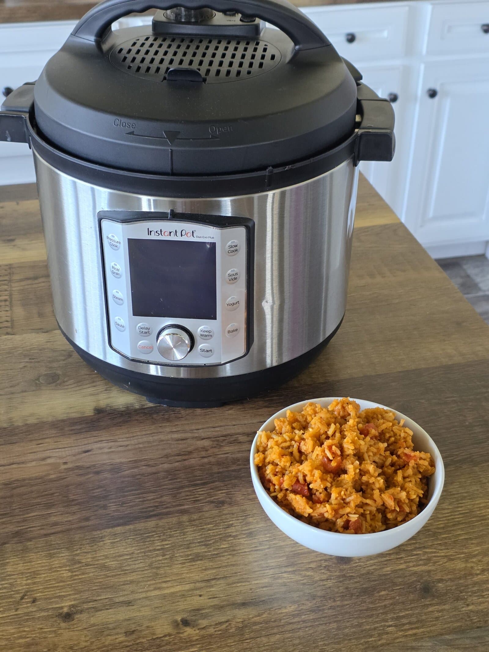 A delicious bowl of Mexican rice served next to a modern rice cooker on a wooden kitchen countertop.