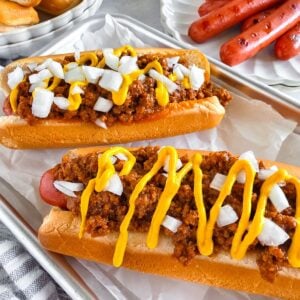A delicious hot dog with savory chili sauce topped with chopped onions and mustard.