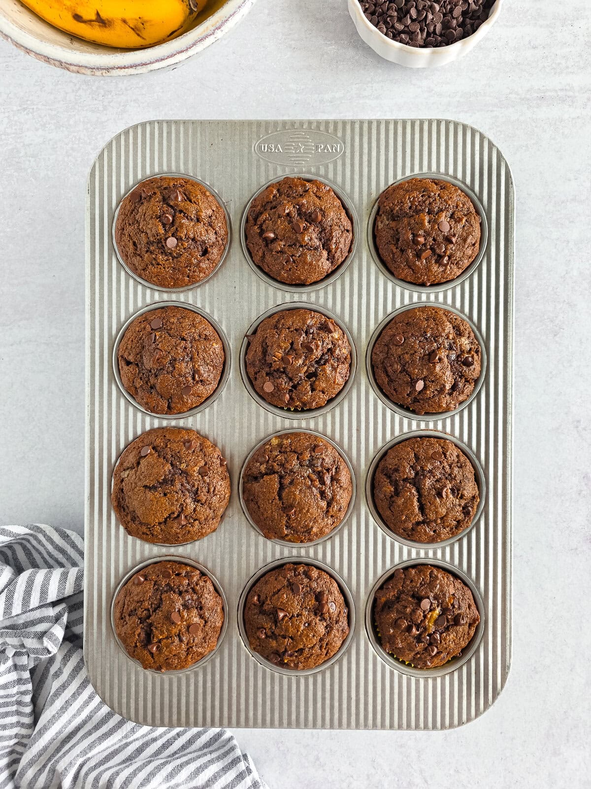 Delicious homemade chocolate chip muffins in a metal baking tray on a white surface.