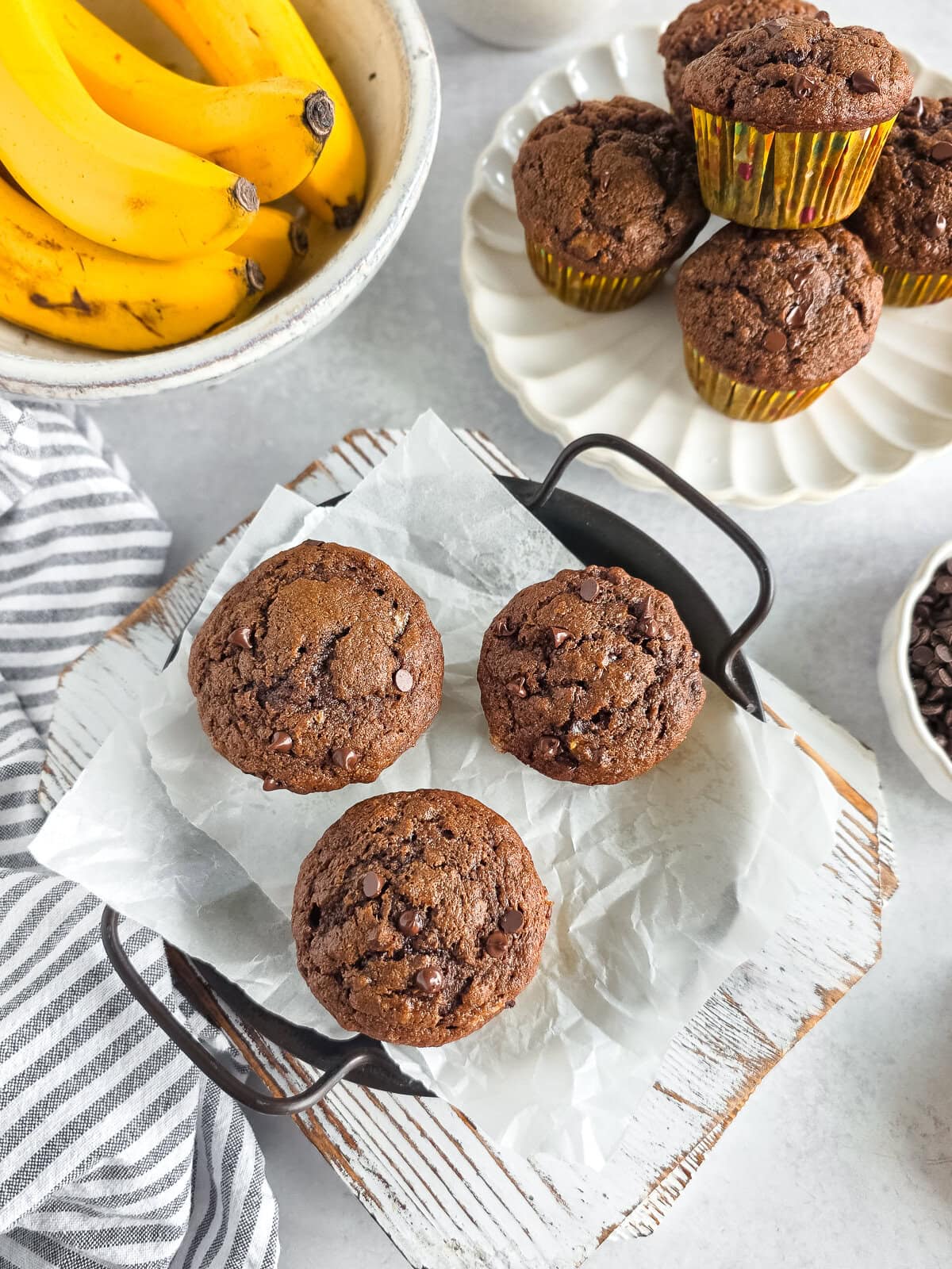 Banana chocolate chip muffins and chocolate cupcakes on a white plate and baking tray.