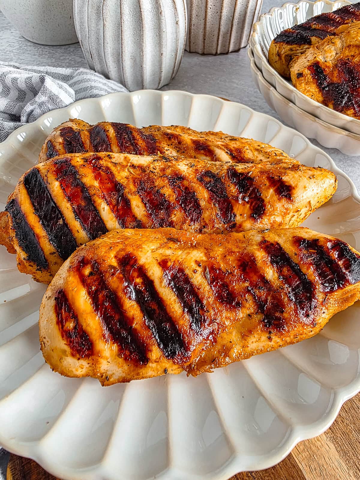 Grilled chicken breasts with char marks on a white scalloped plate, close-up.