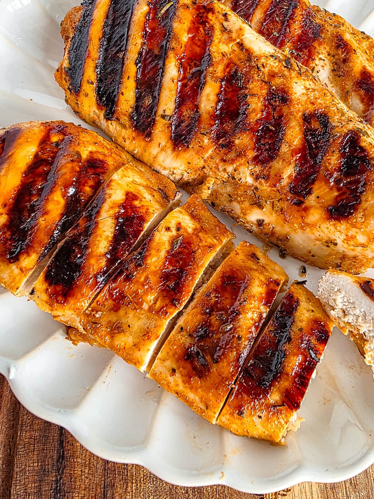 Grilled chicken breast with barbecue sauce, sliced on a white plate.