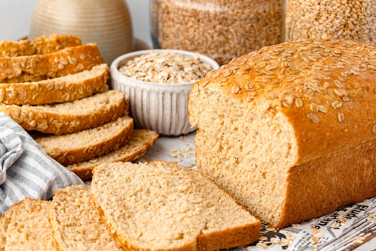 Whole wheat bread loaf with sliced bread and oats in the background.