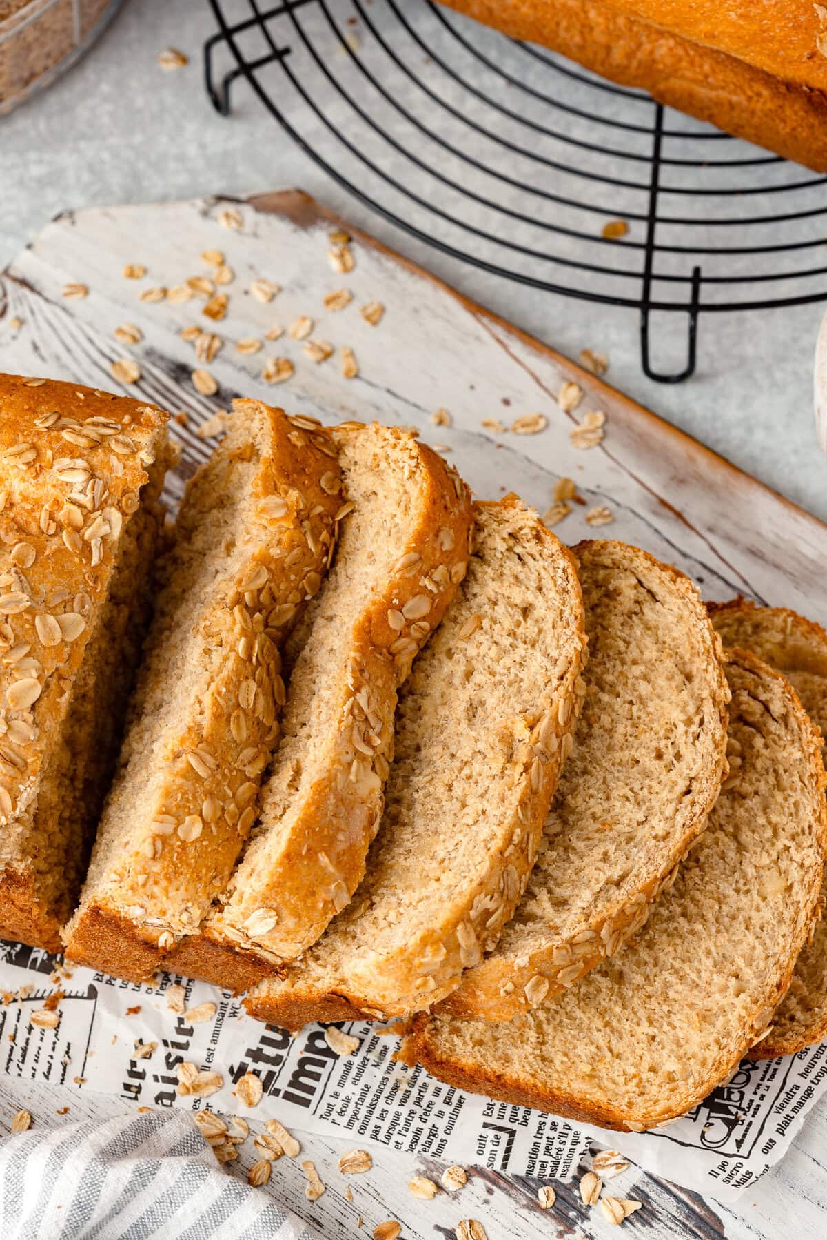 Golden oat bread slices on parchment paper with a loaf in the background.