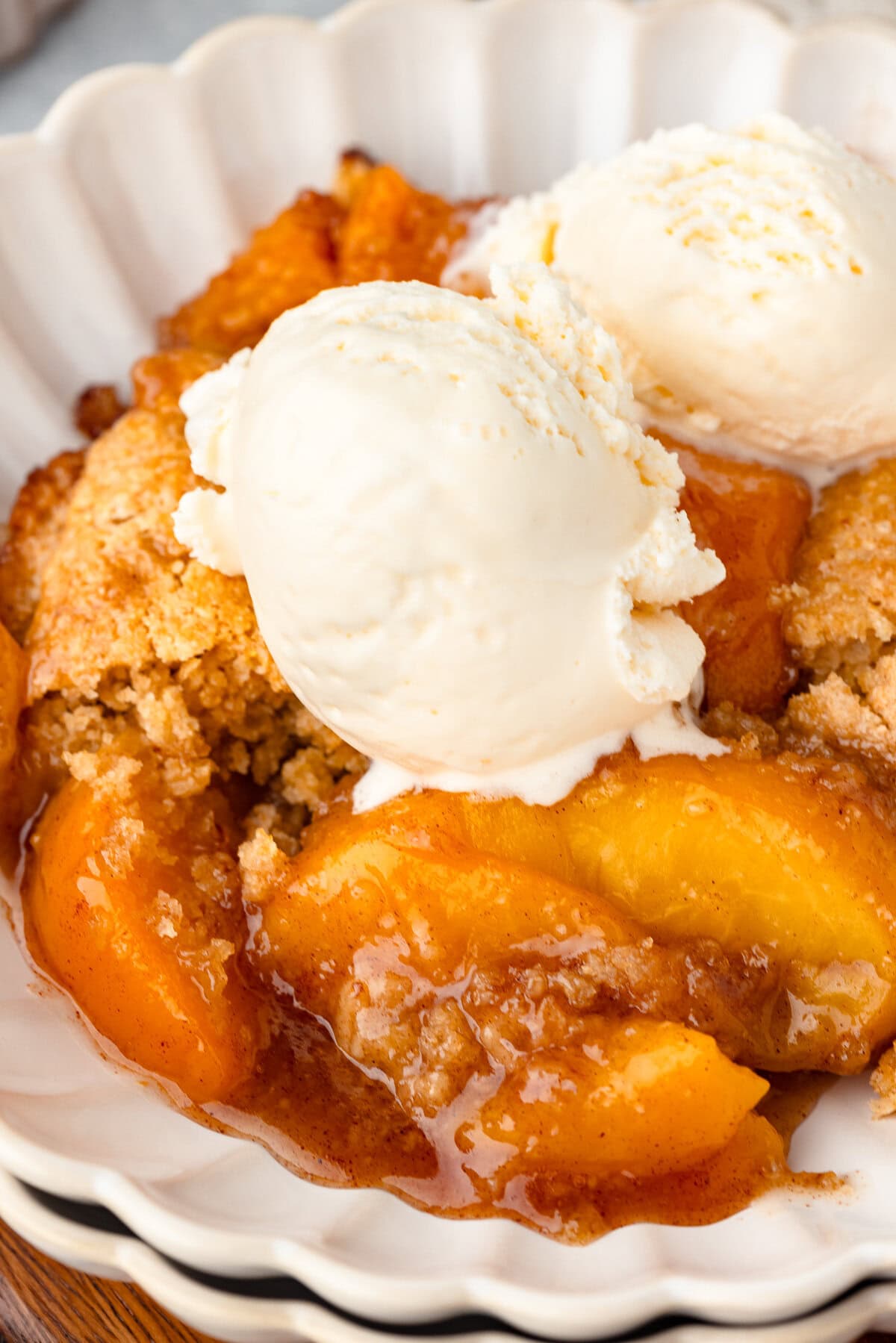 Golden peach cobbler with freshly milled flour with vanilla ice cream on top in a white bowl.