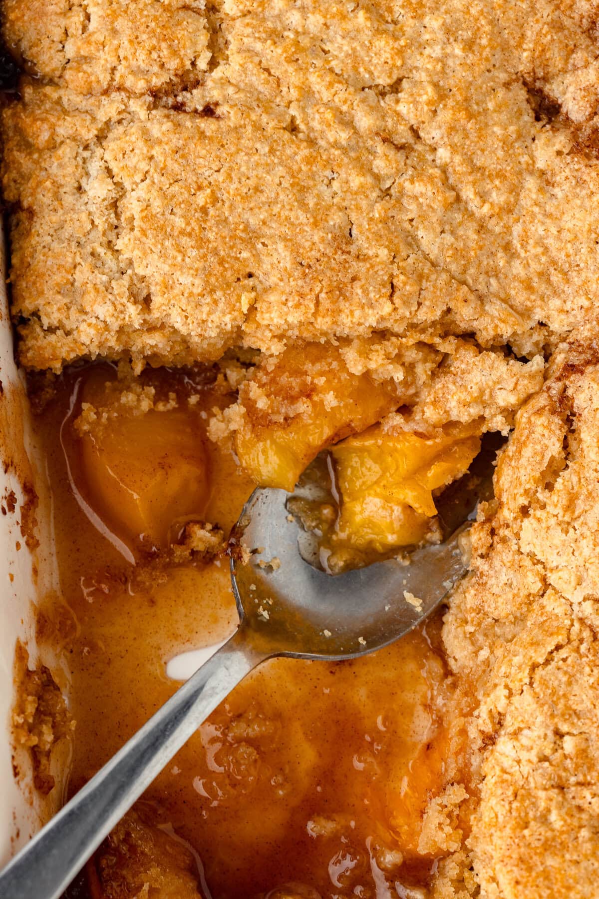 Golden peach cobbler with a crumbly topping and spoonful of warm fruit filling.