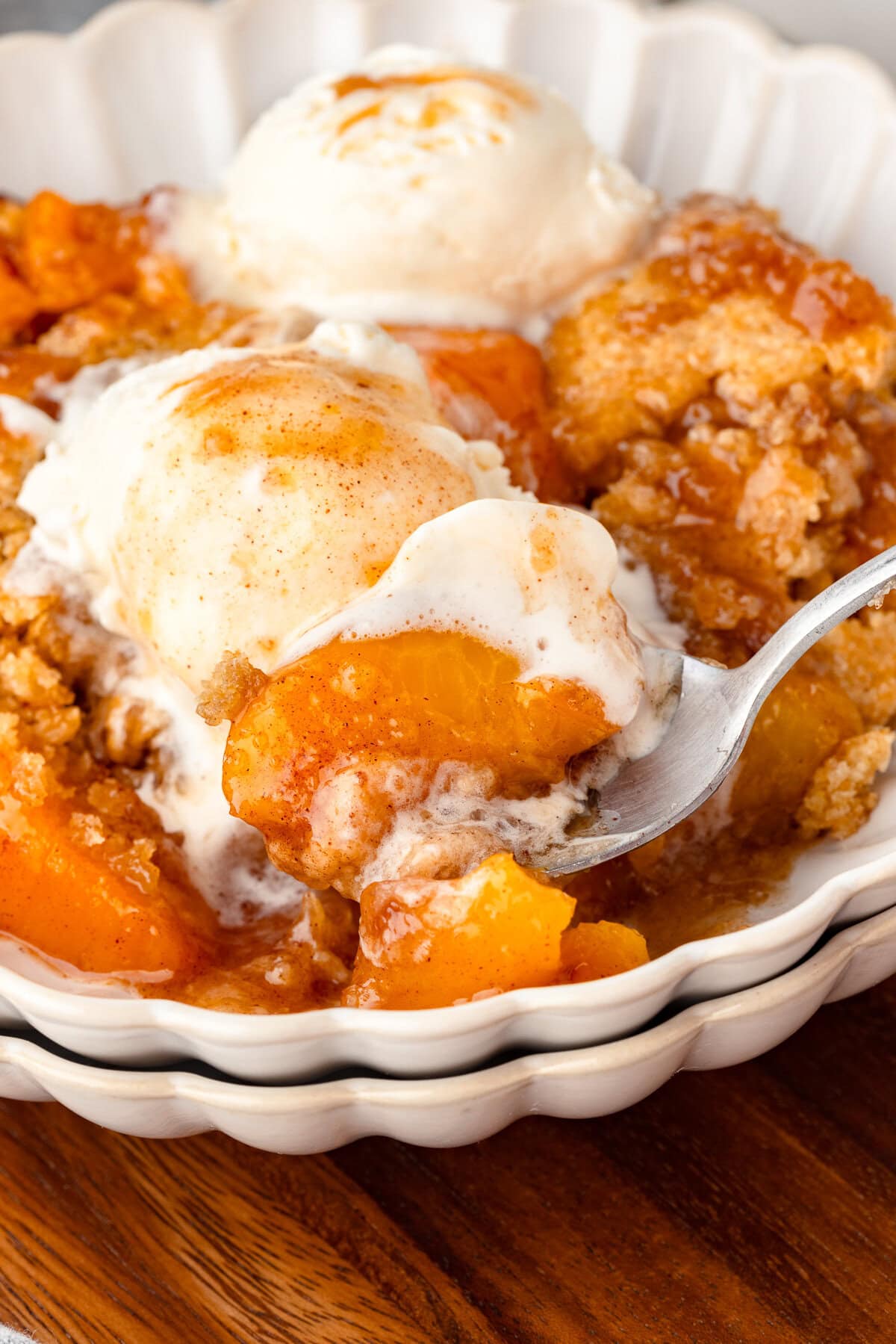 Creamy peach cobbler with vanilla ice cream and whipped cream in a white bowl.