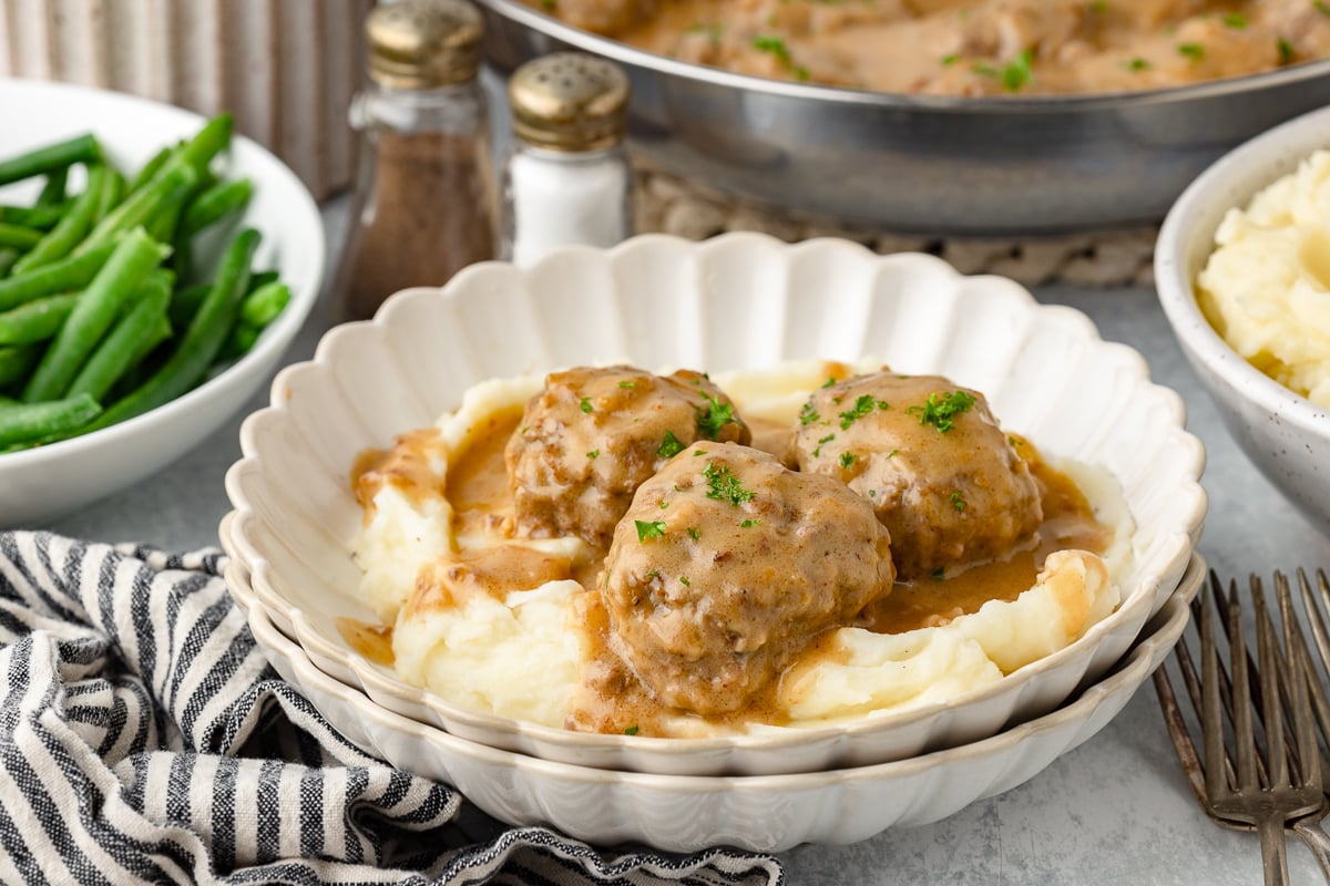 Meatballs and gravy served over creamy mashed potatoes with green beans on the side.
