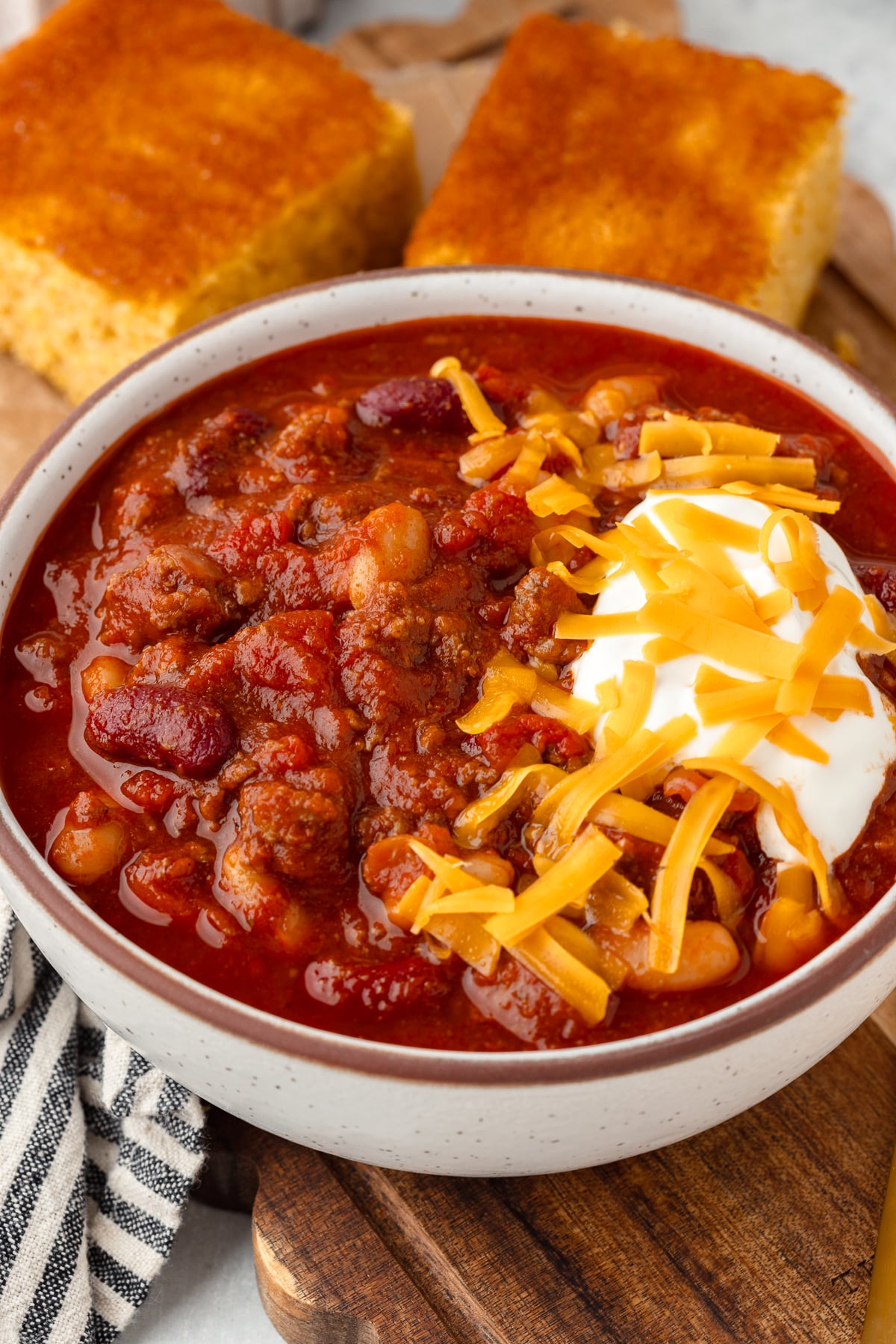 A bowl of chili with beans, topped with cheddar cheese and sour cream.